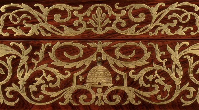 An inlaid and engraved brass design consisting of scrollwork, foliation, bees and bee skeps (beehives) from an antique jewellery box in rosewood.