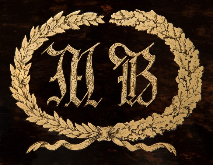 Engraved foliate wreath emblem encircling the initials 'M.B', from an antique jewellery box in coromandel with engraved brass inlay.